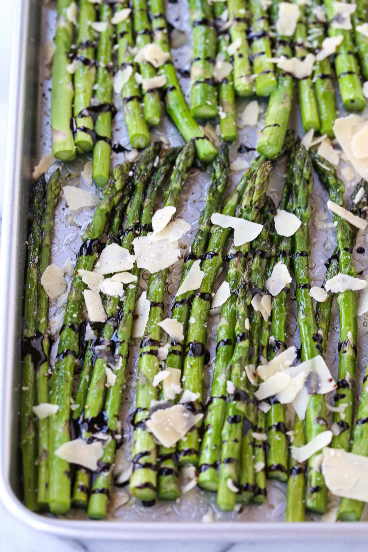 roasted asparagus on a sheet pan with parmesan cheese and balsamic glaze
