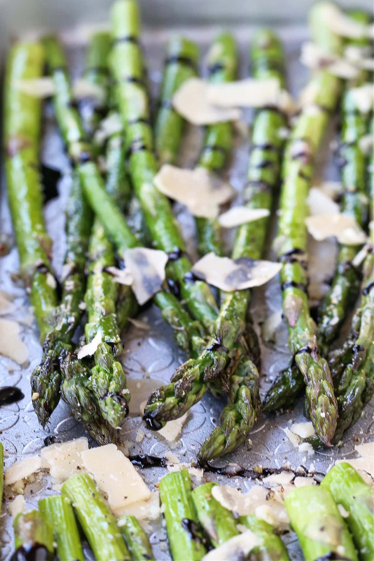 asparagus on a sheet pan with shaved parmesan cheese and balsamic glaze