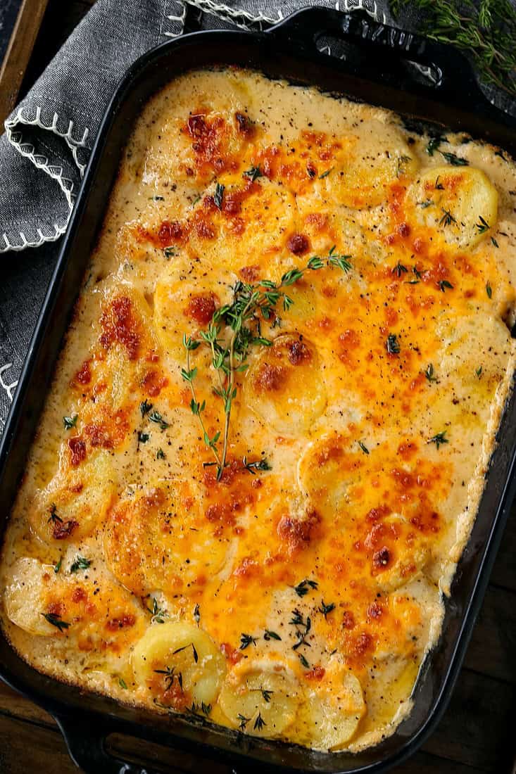 scalloped potato recipe in a black baking dish with fresh thyme