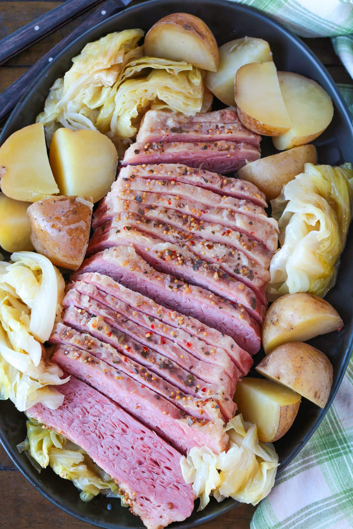 sliced corned beef on a black platter with potatoes and cabbage