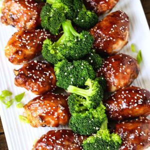 Baked chicken legs with an Asian glaze on a white platter with broccoli
