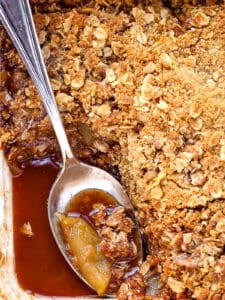 apple crisp in a baking dish with spoon and sauce