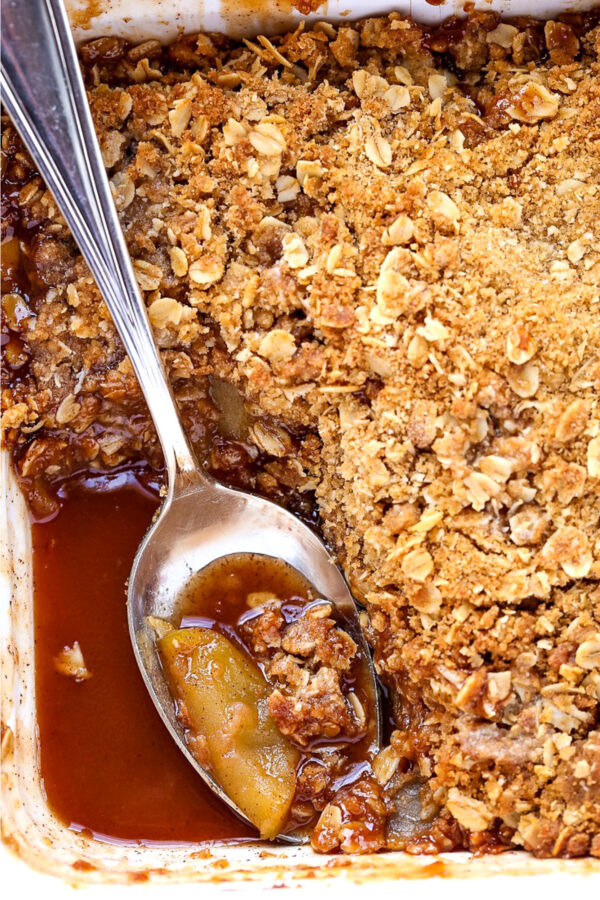 apple crisp in a baking dish with spoon and sauce