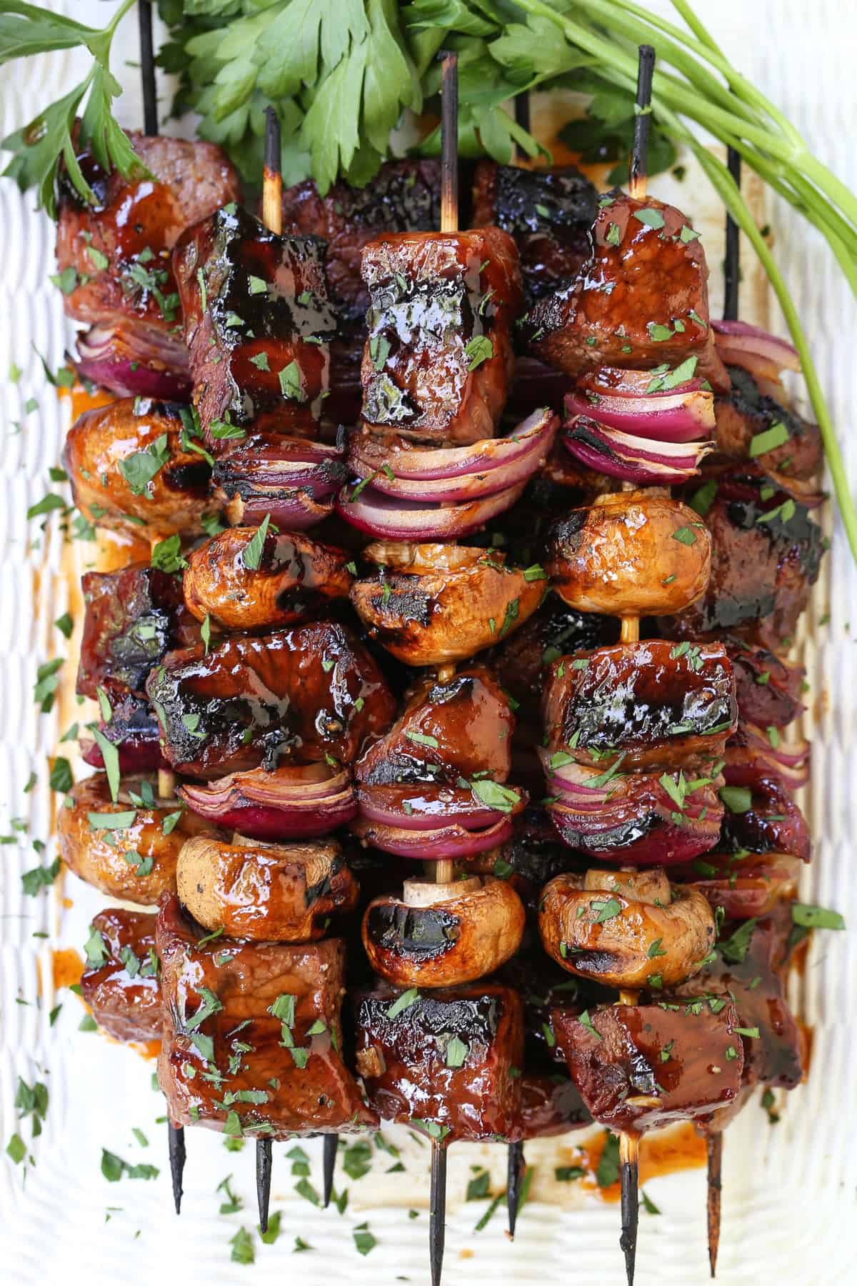 Steak and vegetable kabobs stacked on white platter