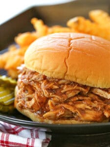 shredded barbecue chicken on a bun with fries