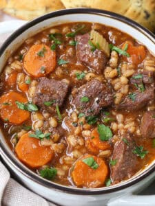 beef barley soup in a white crock with rolls