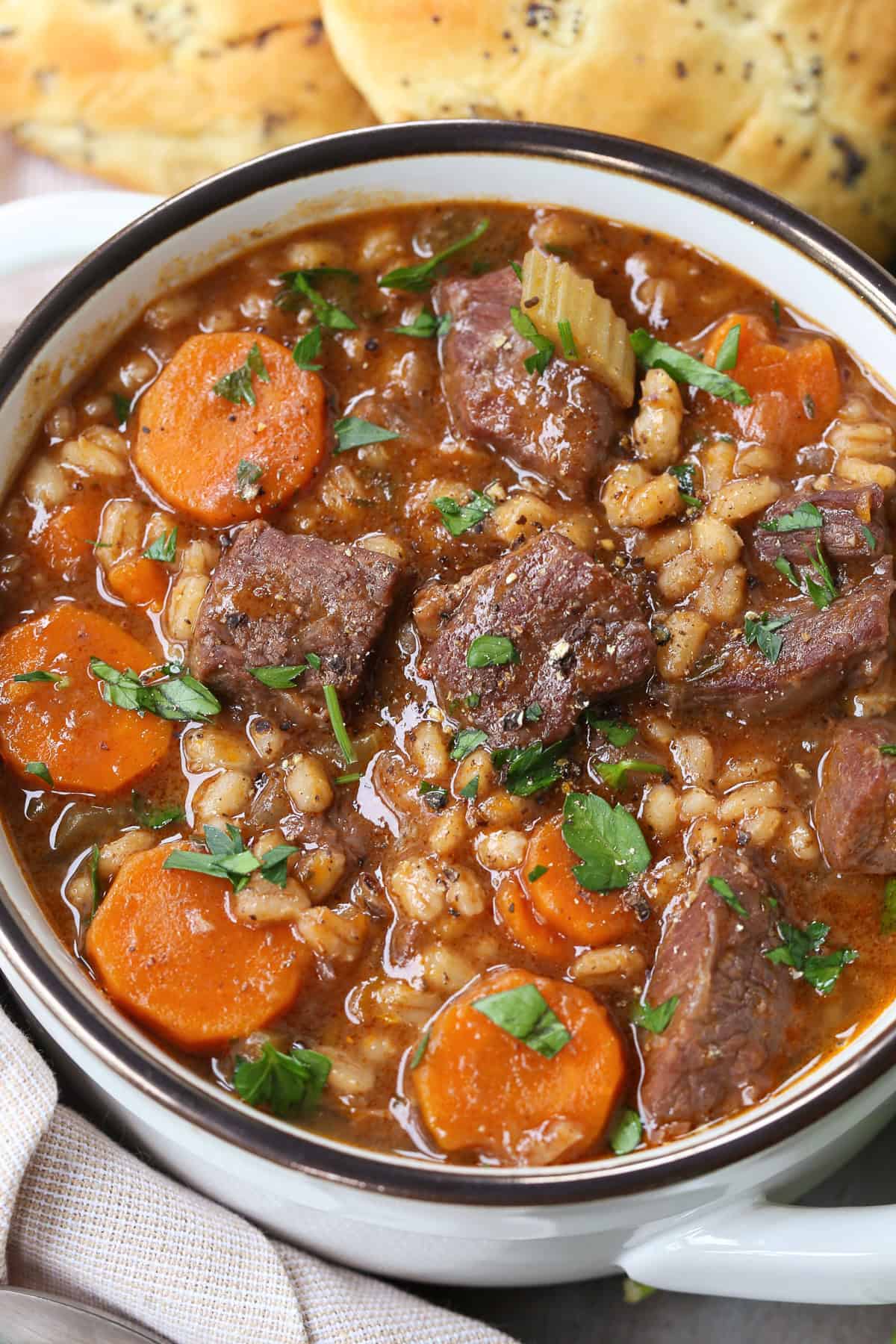 beef barley soup in a white crock with rolls