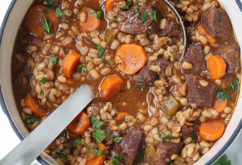 beef soup with vegetables and barley in pot with ladle