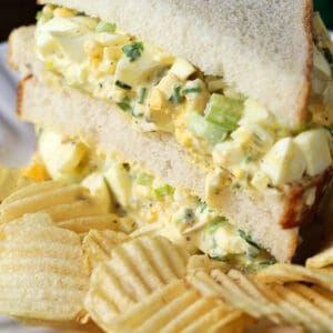 Egg salad on white bread cut in half with chips