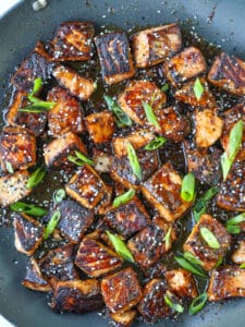 salmon bites in a skillet with scallions and sesame seeds