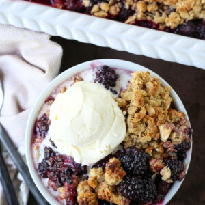 blackberry crispy in a bowl with vanilla ice cream and baking dish in background