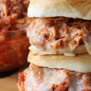 Shredded chicken sandwiches stacked on a board with cheese