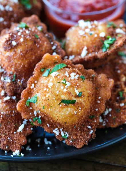 Close up of a fried ravioli with parsley and parmesan cheese on it, with more ravioli in the background