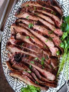 sliced flank steak on platter with parsley