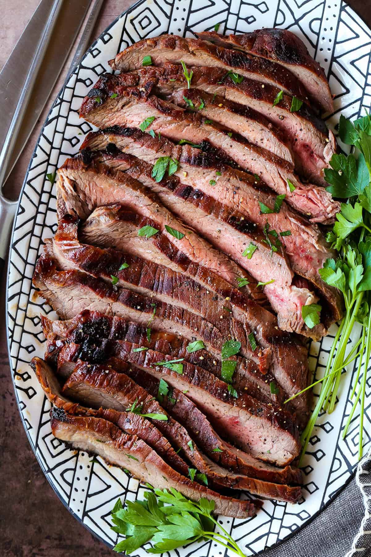 sliced flank steak on platter with parsley