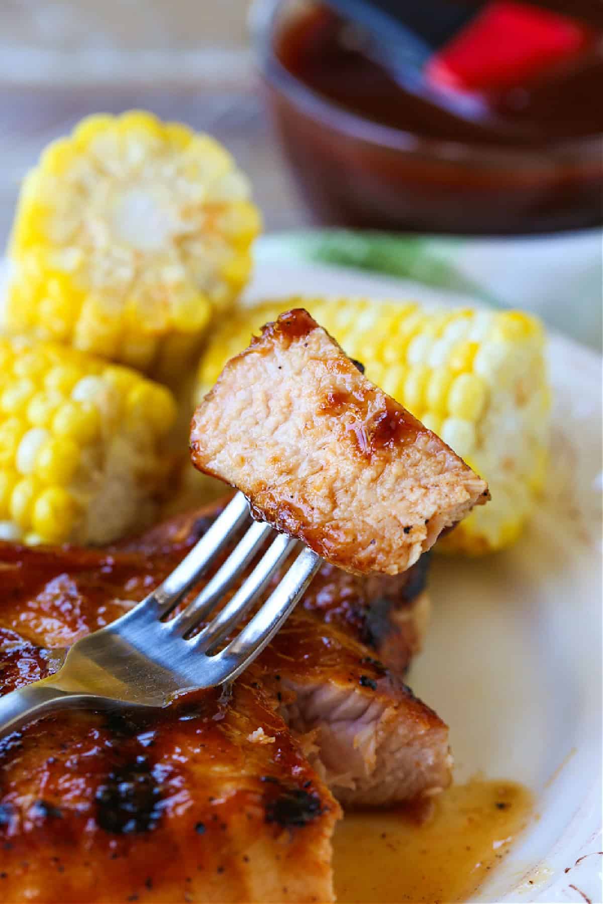 fork with bite of pork chop on plate with corn