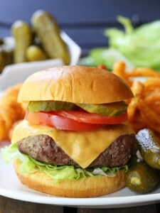 cheeseburger with toppings on plate with pickles and fries