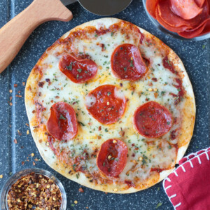 air fryer pizza on board with pizza cutter, pepperoni and napkin
