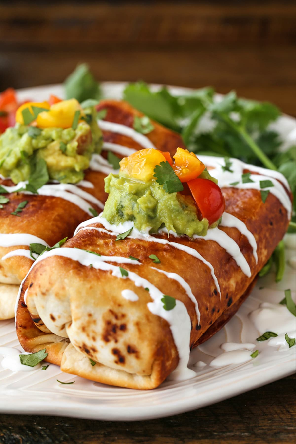 chicken chimichangas on a plate with toppings and sour cream drizzle