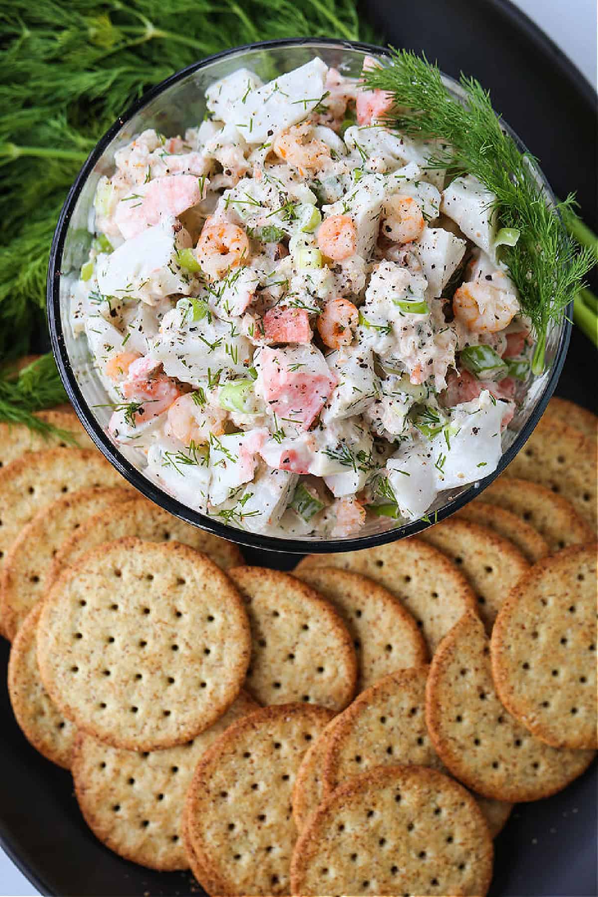 cold seafood salad in bowl with fresh dill and crackers
