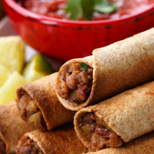 beef taquitos stacked on a plate with salsa