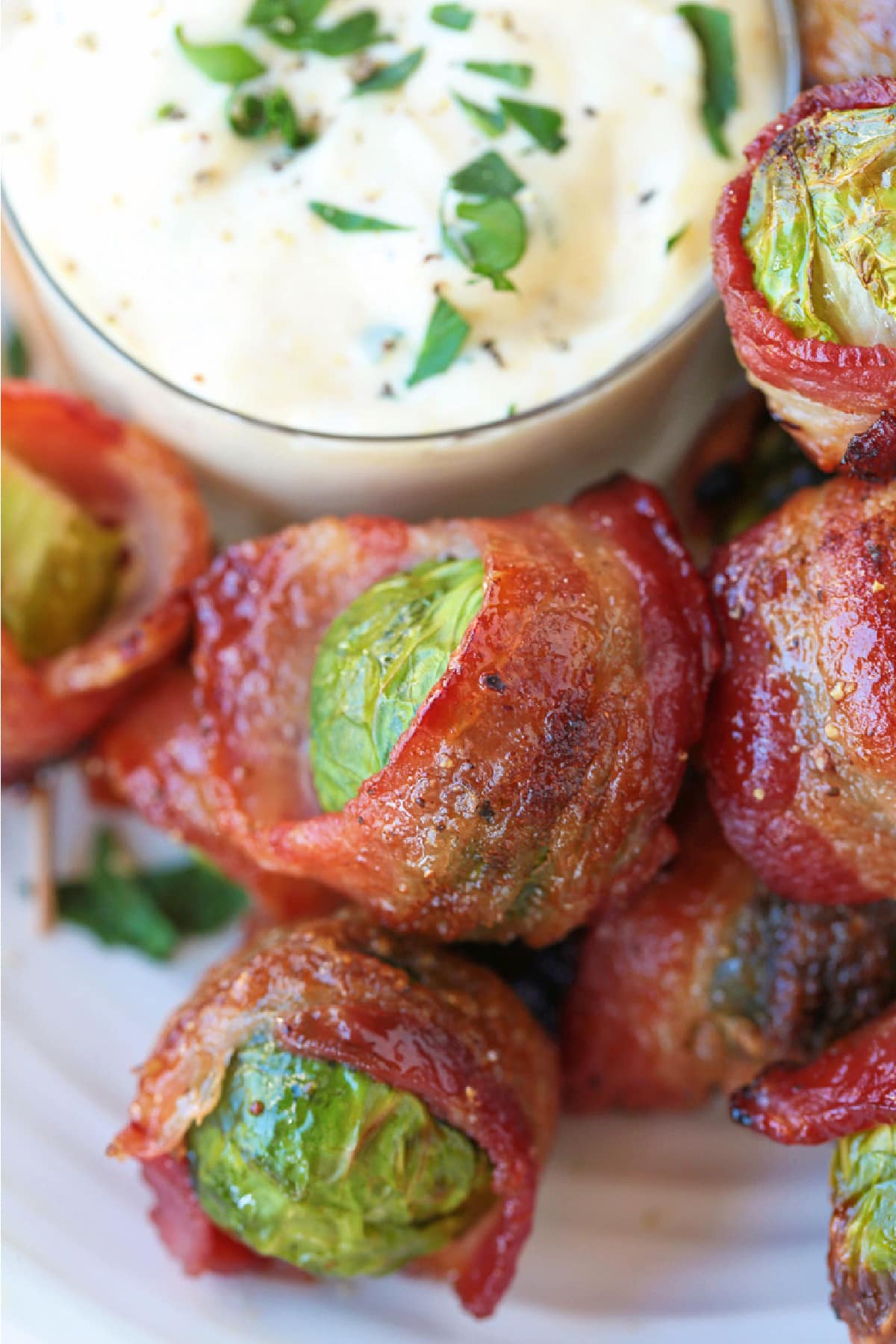 close up of bacon wrapped brussels sprouts on plate with garlic aioli