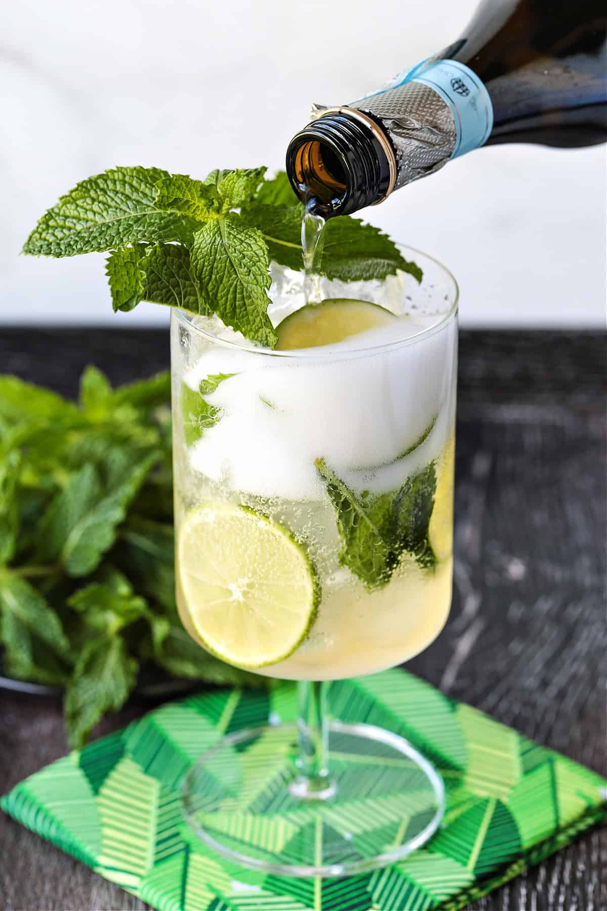 prosecco being poured into a glass with mint and limes