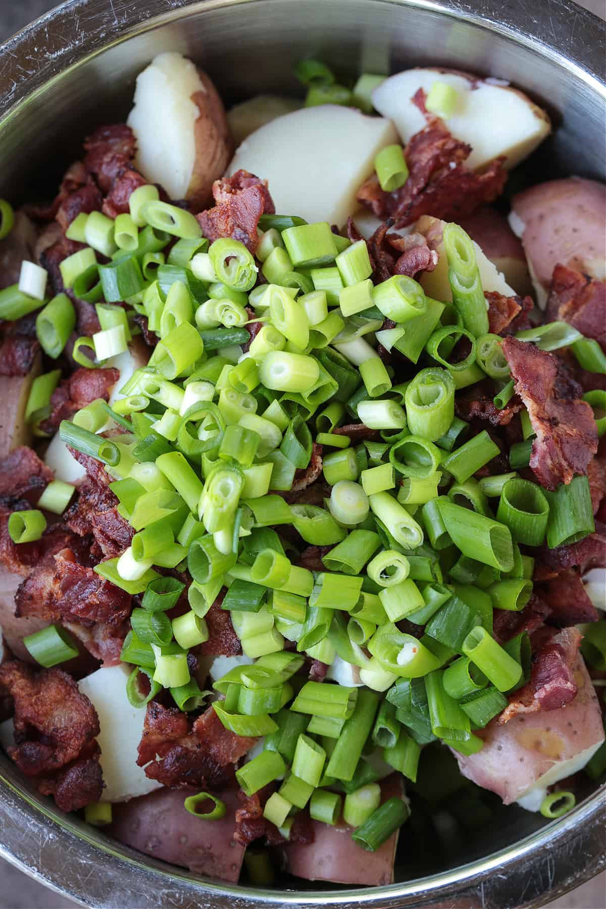 chopped scallions and bacon in a bowl with potatoes