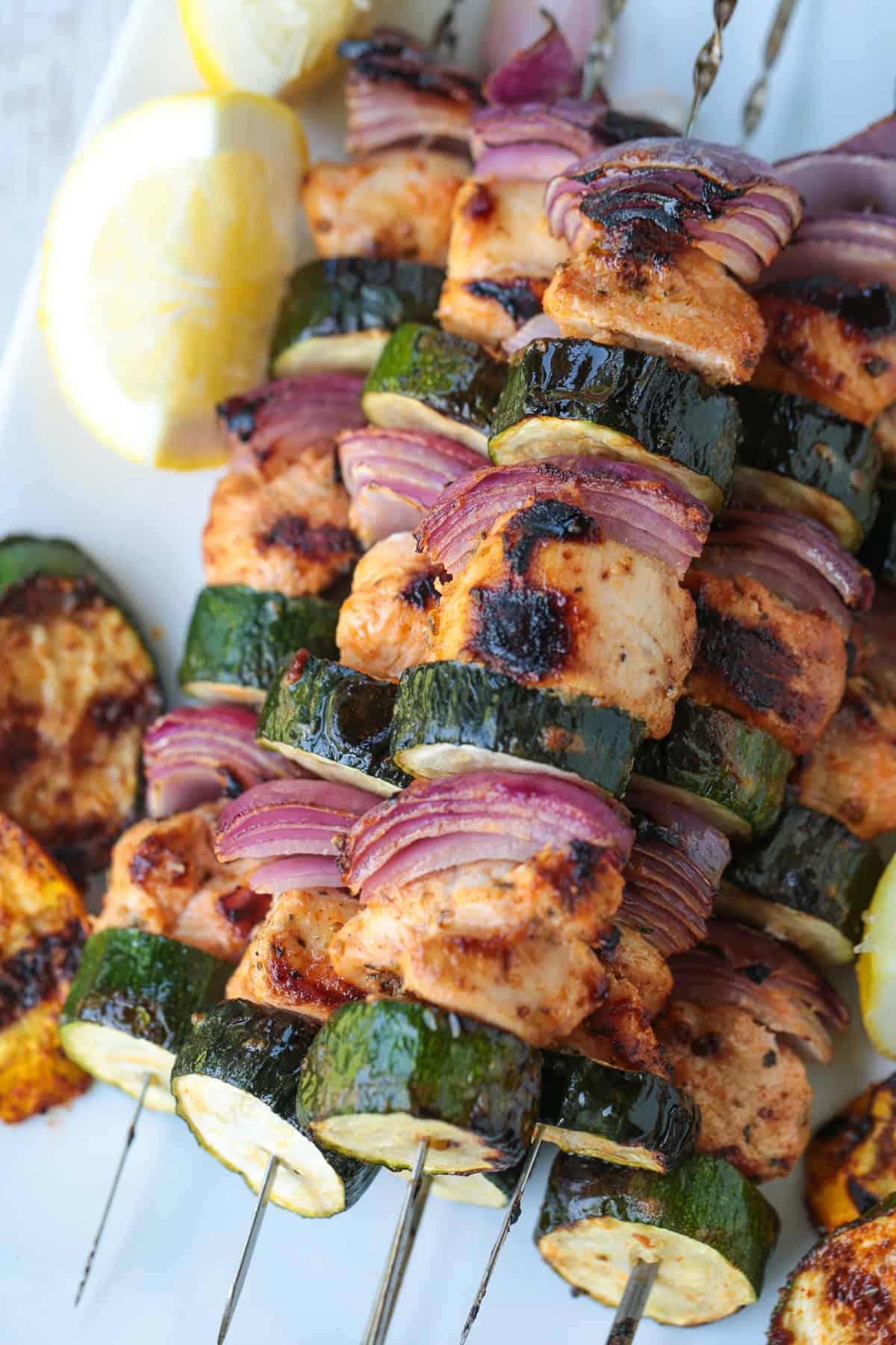 greek chicken kabobs on white platter with grilled vegetables and lemons