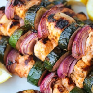 greek marinated chicken kabobs with vegetables stacked on plate