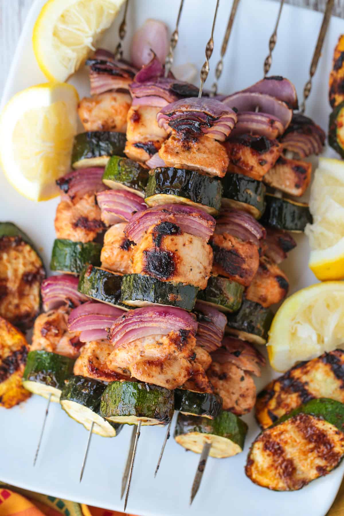 greek chicken kabobs stacked on a white platter with lemons