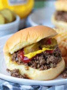 loose meat sandwich on bun with pickles, ketchup and mustard