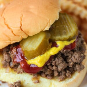 loose ground beef sandwich on a bun with pickles, mustard and ketchup