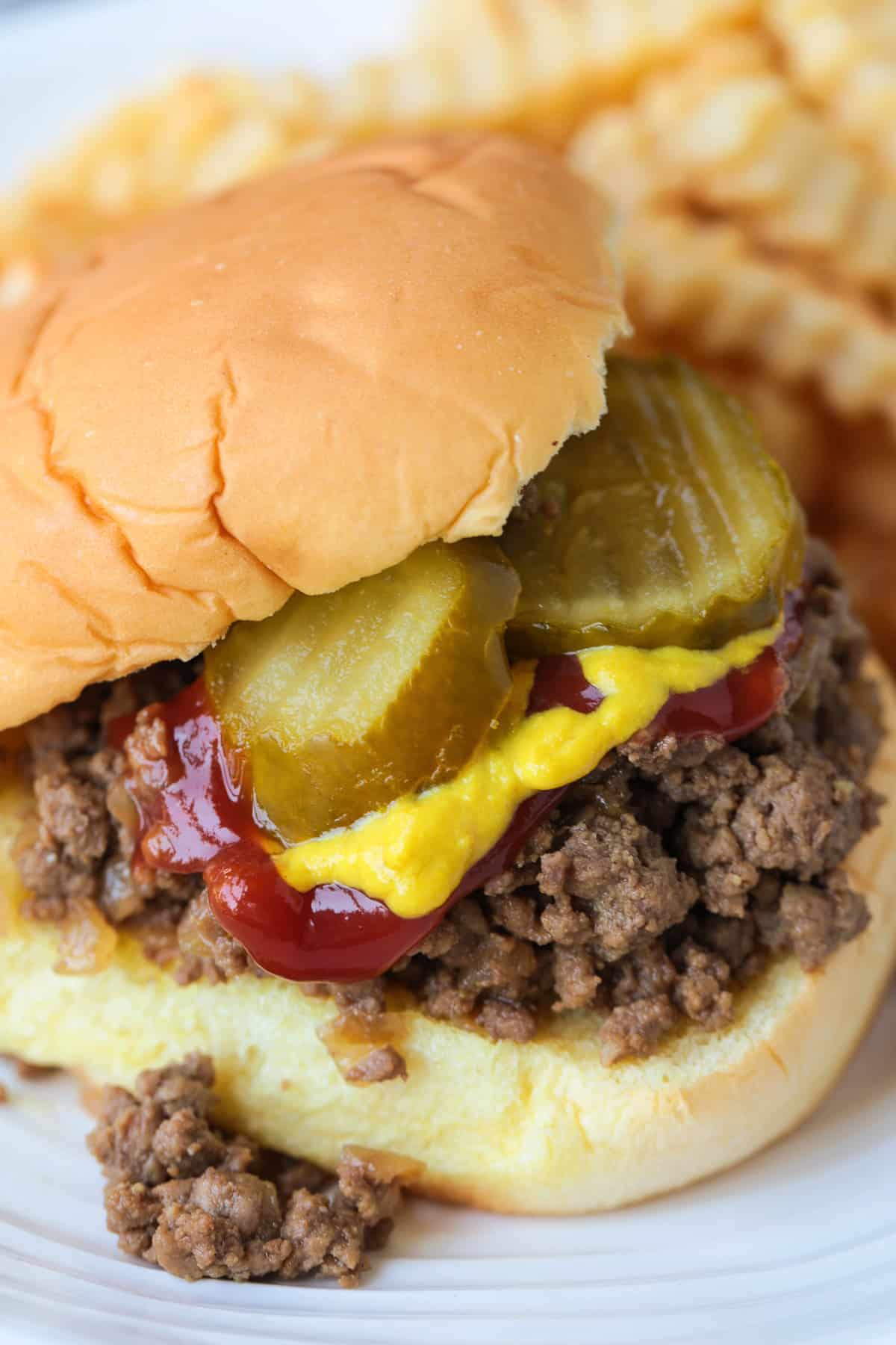 loose ground beef sandwich on a bun with pickles, mustard and ketchup