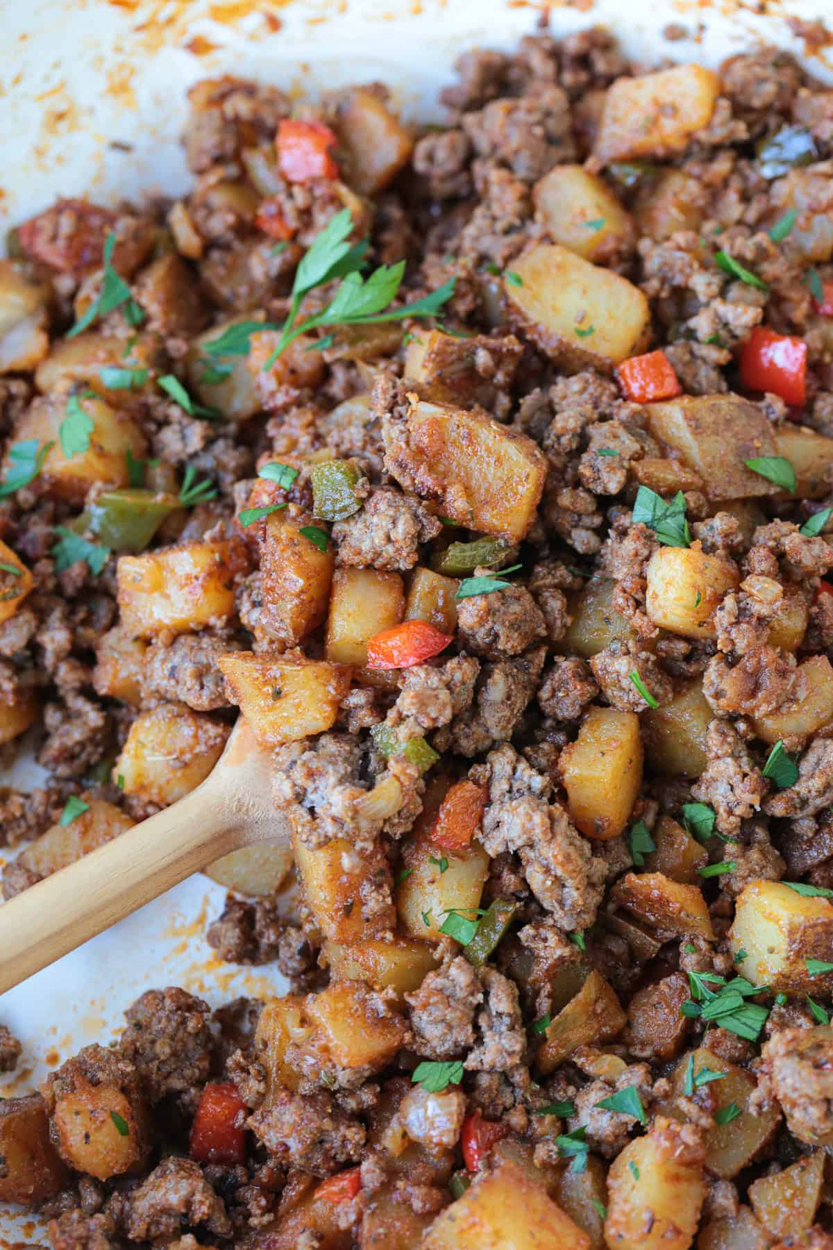 ground beef with potatoes and peppers in a skillet with wooden spoon