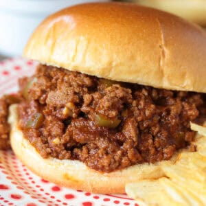 sloppy joe sandwich on a plater with chips and pickles