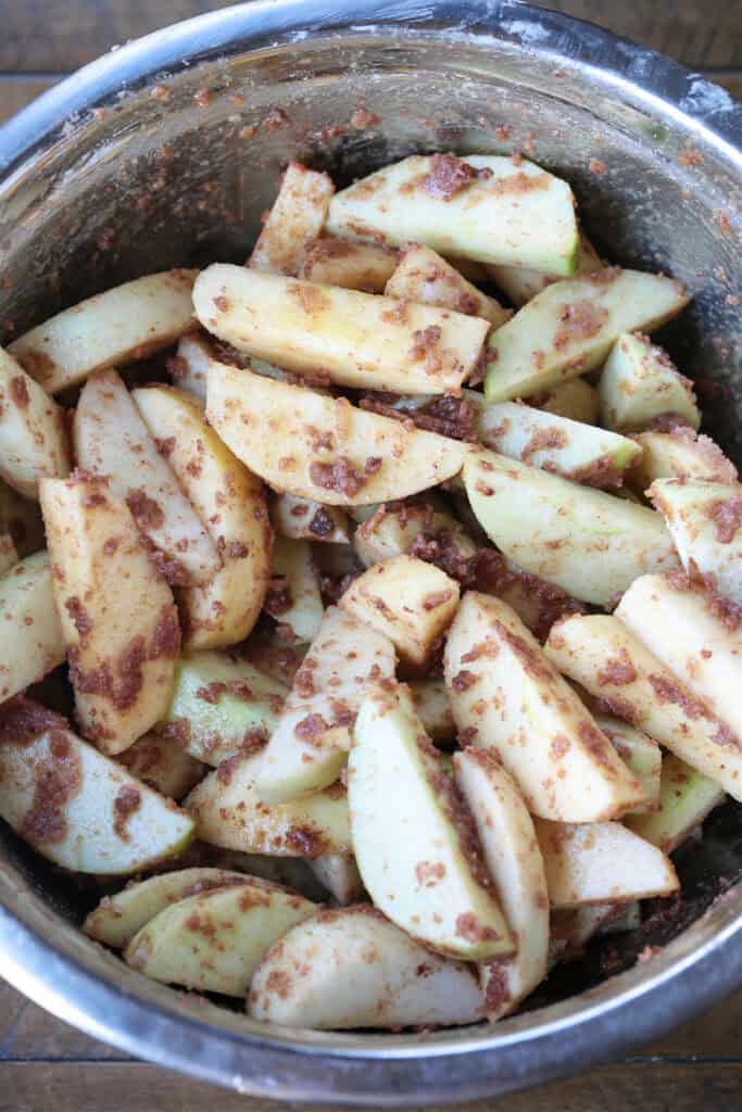 sliced apples tossed in a bowl with brown sugar and cinnamon