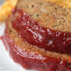 sliced meatloaf with ketchup glaze stacked on a plate with fries