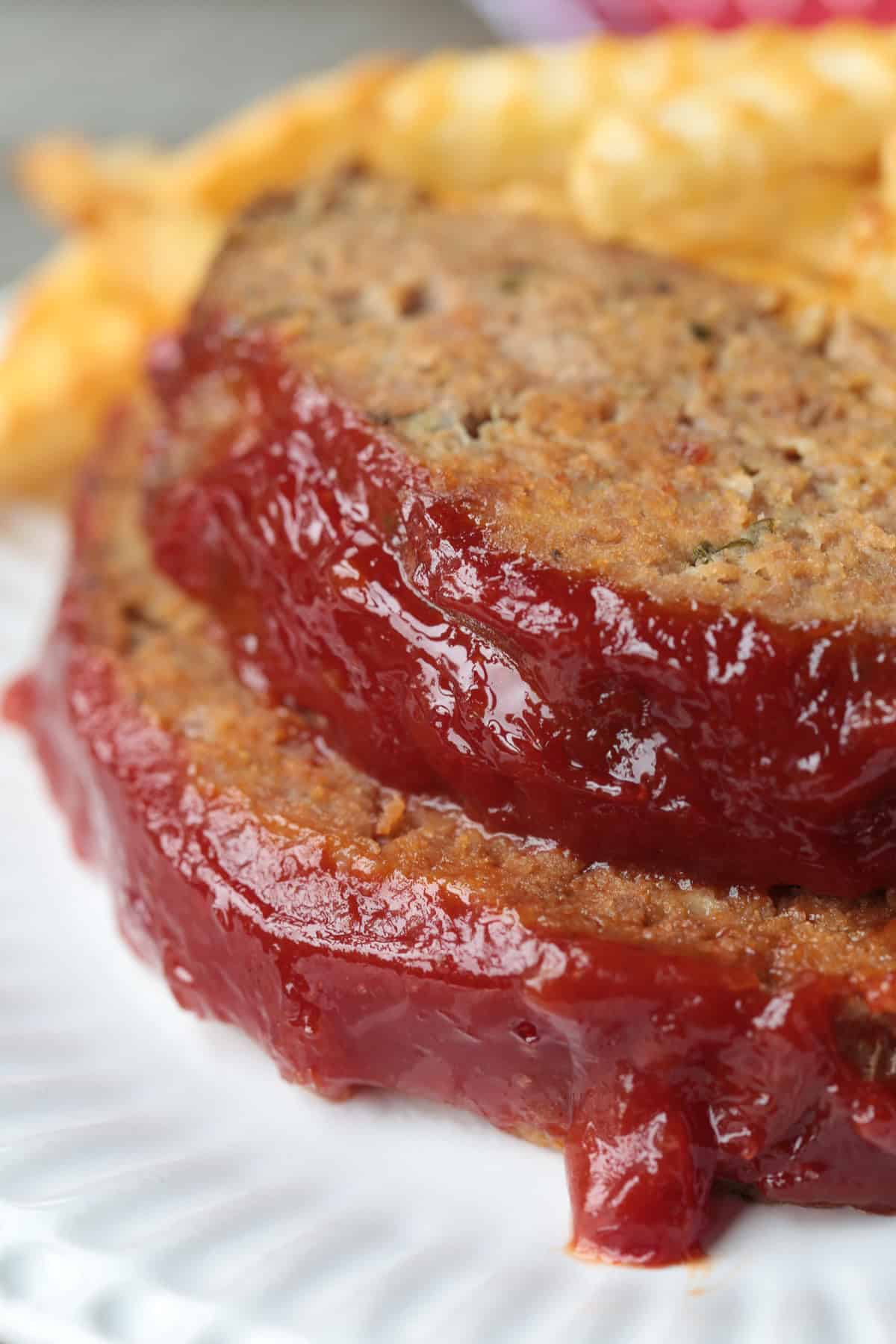 sliced meatloaf with ketchup glaze stacked on a plate with fries